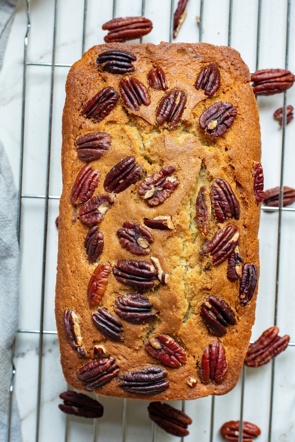 Overhead shot of banana bread on a cooling rack with pecans on top. 