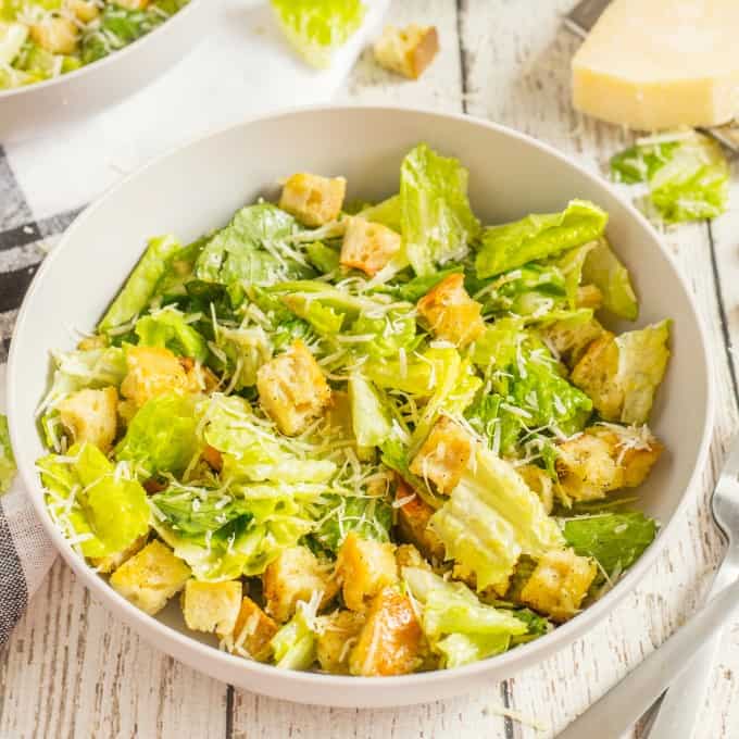 White bowl full of Caesar salad on a white board