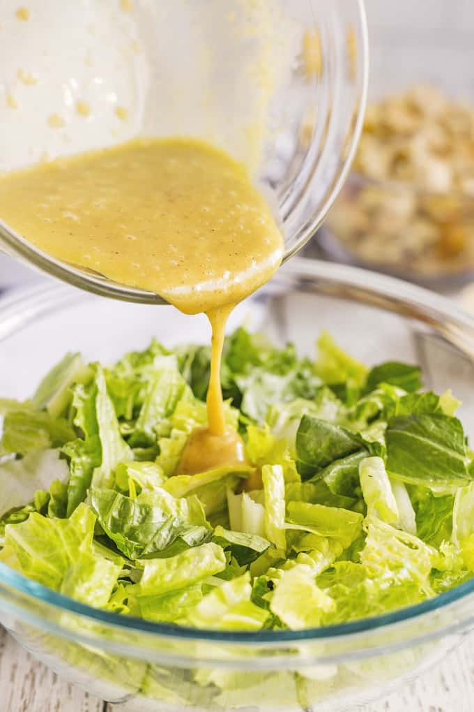 Romaine lettuce pieces in a clear bowl with the Casear dressing being poured on top