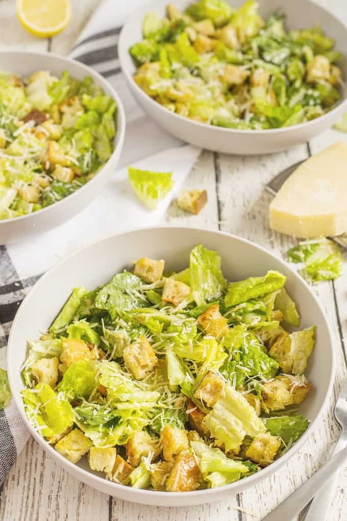 3 serving bowls of Caesar Salad on a wooden board 