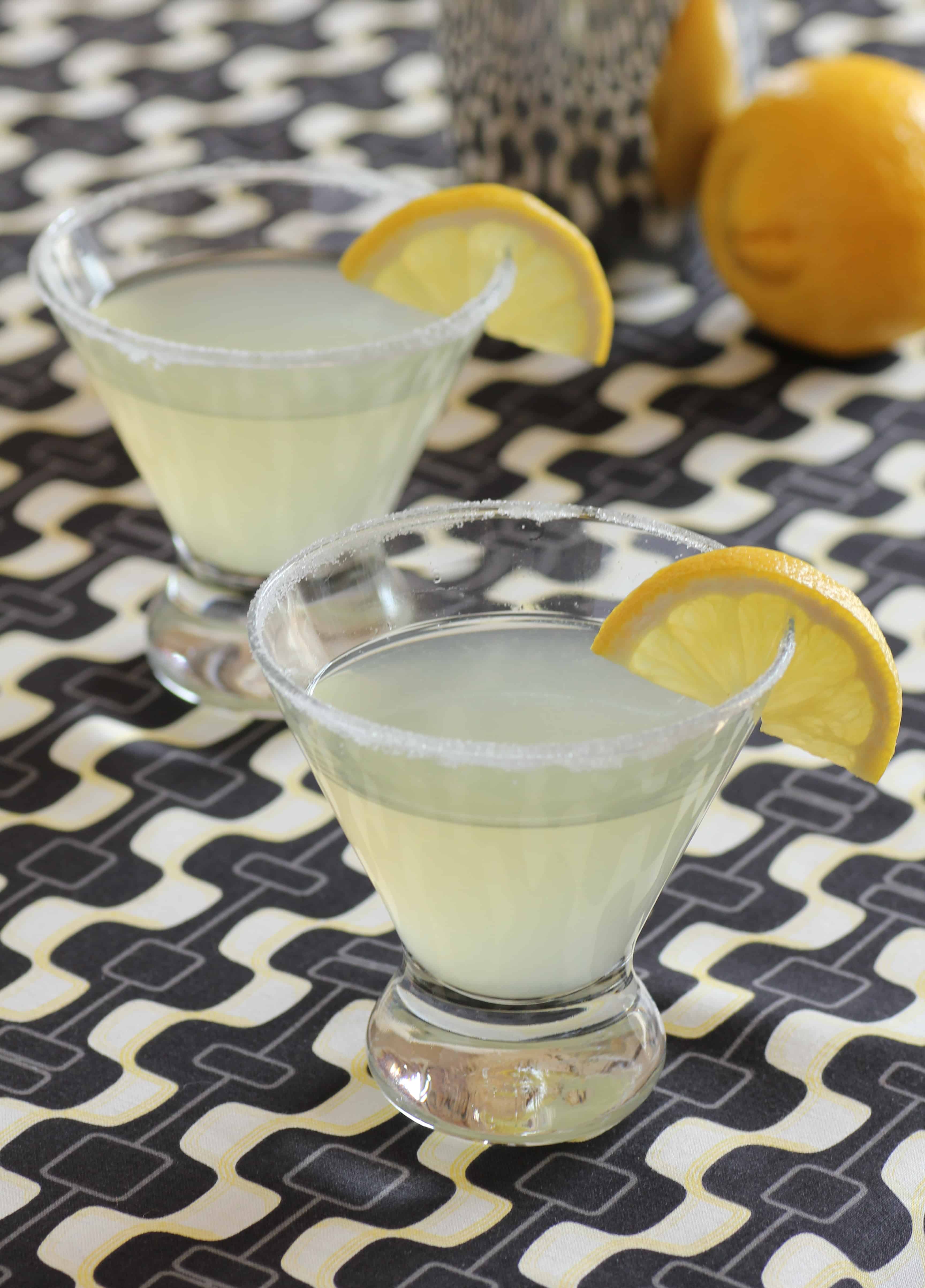2 glasses of lemon drop cocktail on a patterned table cloth with lemon slice as garnish