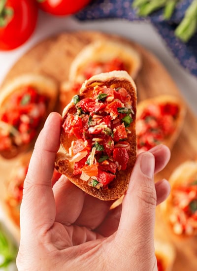 Holding a slice of bruschetta.