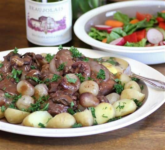 Coq Au Vin on an oval platter with potatoes, garnished with parsley