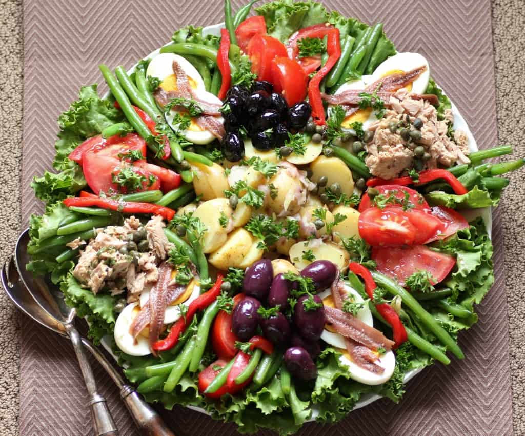 Salade Nicoise on a large round platter with serving spoons on the side.