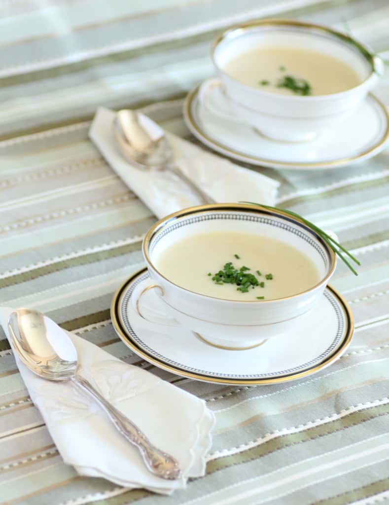 Julia Child's Vicyssoise soup garnished with chopped chives in a white china soup bowl with a silver soup spoon and napkin