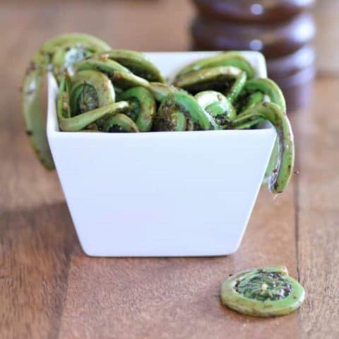 Sauteed Fiddleheads in a square white bowl on a wooden board