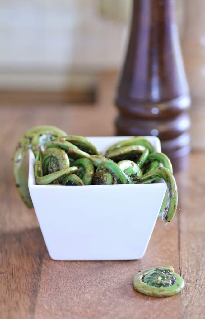Sautéed Fiddleheads in a small white square bowl on a wooden cutting board