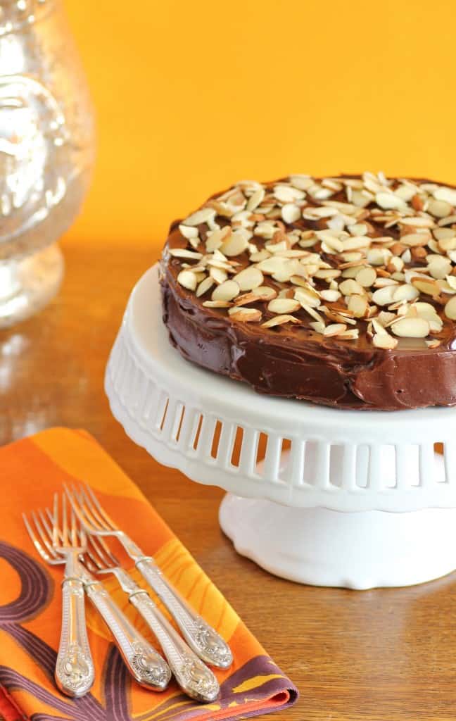 Reine De Saba chocolate cake on a white cake stand with forks and napkins on the table