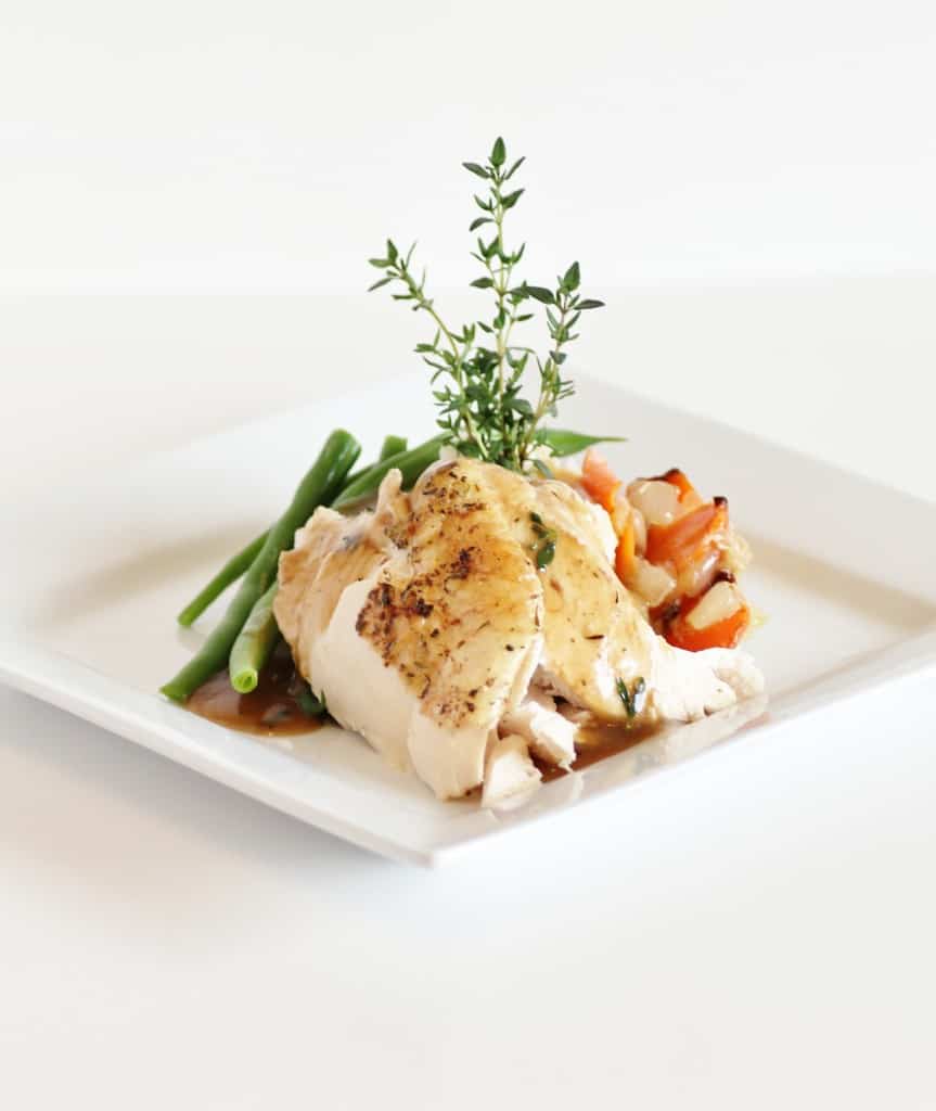 Roasted Chicken pieces on a white plate with green beans peppers, and a sprig of thyme