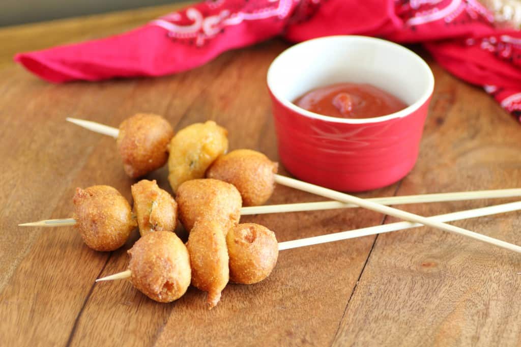 Cowboy Corndogs with a Twist on wooden skewers with a bowl of ketchup for dipping