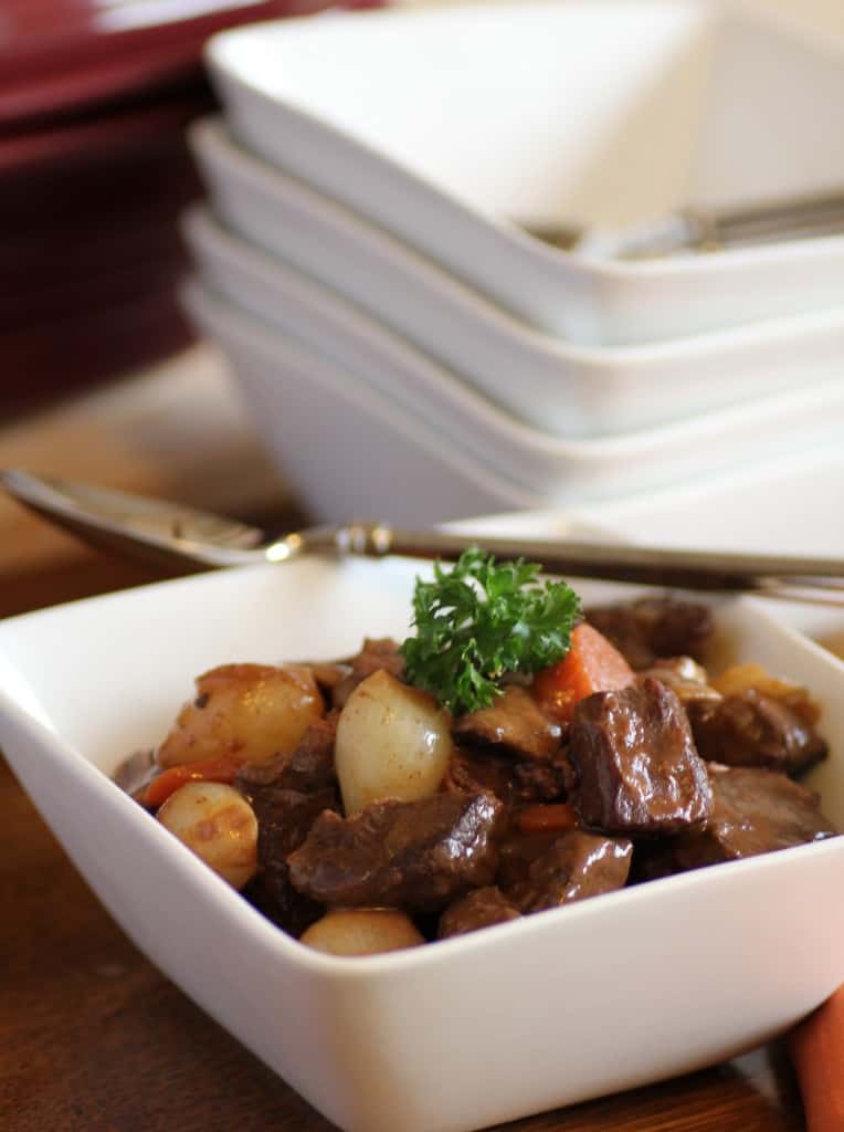 Boeuf Bourguignon in a white bowl with a spoon and other white bowls in the background