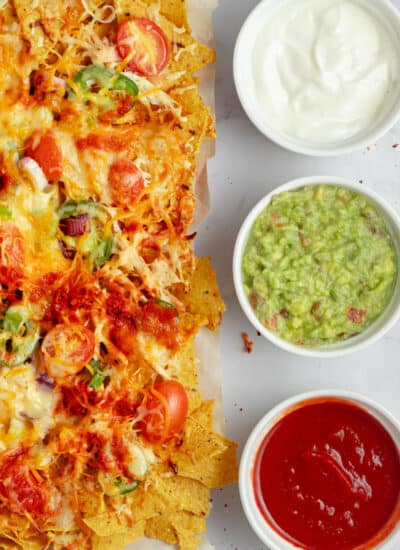 Nachos on the left with bowls of sour cream, guacamole and salsa down the side.