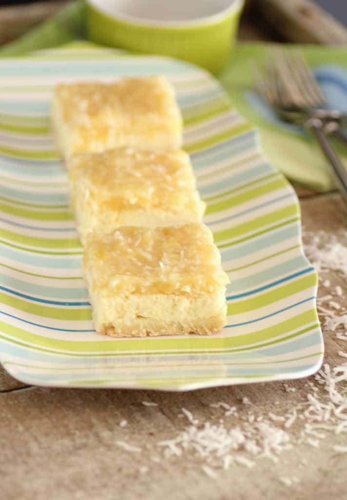 3 Pina Colada Cheesecake Squares on a colourful platewith shredded coconut around the plate