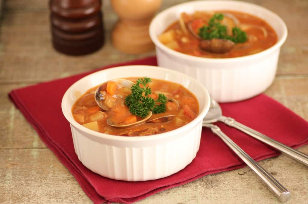 2 bowls of Manhattan Clam Chowder on a wooden board with 2 spoons