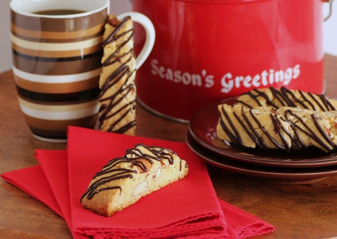 Amaretto Almond Biscotti pieces on a small brown plate and one on a red napkin with a coffee mug