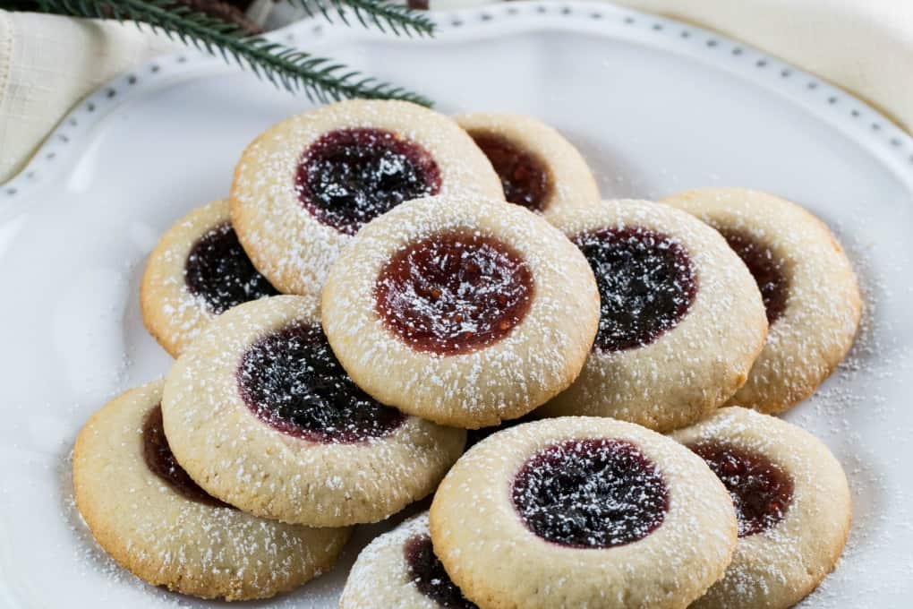 Thumbprint Cookies on a white plate with greenery in the background and on a cream napkin