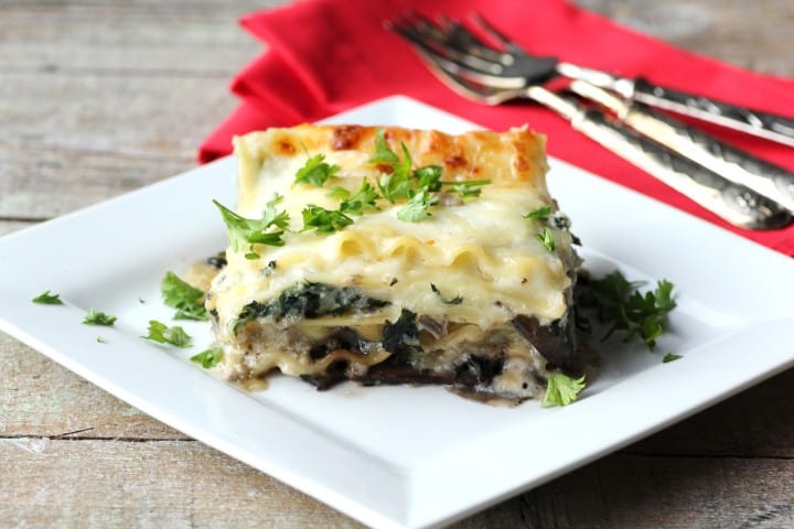 Mushroom, Spinach and Four Cheese Lasagna piece on a white plate with forks and a red napkin