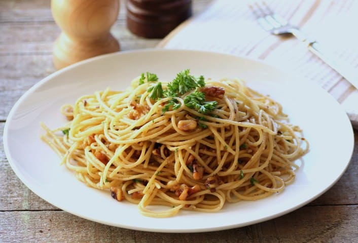 Spaghetti Olio with Walnuts on a white plate sitting on a rough wooden board