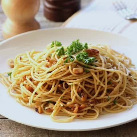 Spaghetti Olie with walnuts on a white plate garnished with fresh parsley