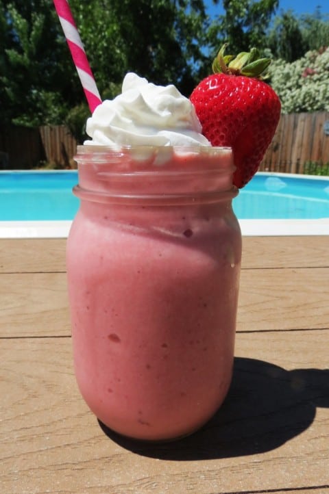 Strawberry Frappe on a table beside the pool, with a straw and strawberry garnish