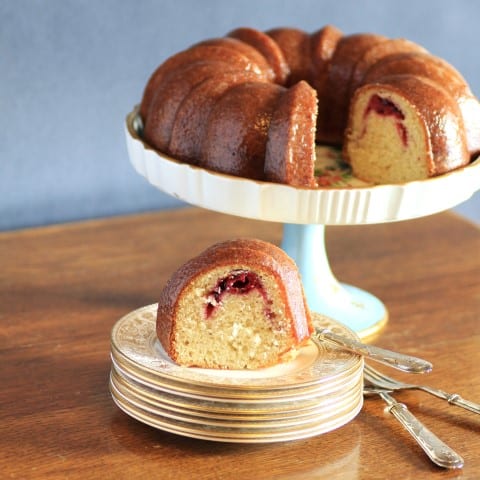 Cherry Kirsch Bundt on a white cake stand with a slice cut out and sitting on a small serving plate