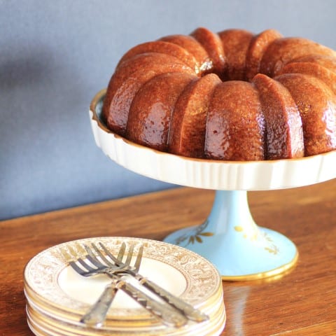 Cherry Kirsch Bundt on a white cake stand with small plates and forks on a wooden table