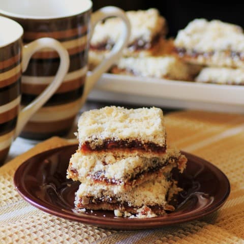 Maple-Date Bars stacked on a small brown plate beside 2 coffee mugs