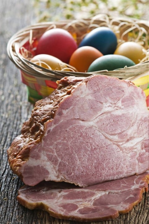 Boneless Ham with Brown Sugar Pineapple Glaze sliced with a basket of coloured Easter eggs