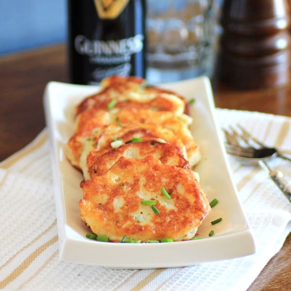 Crispy potato pancakes on a white serving dish with Guinness in the background. 