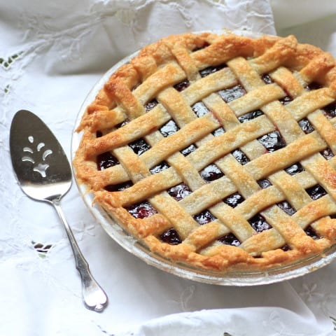 Cherry Blueberry Pie on a white tablecloth with a silver serving spoon