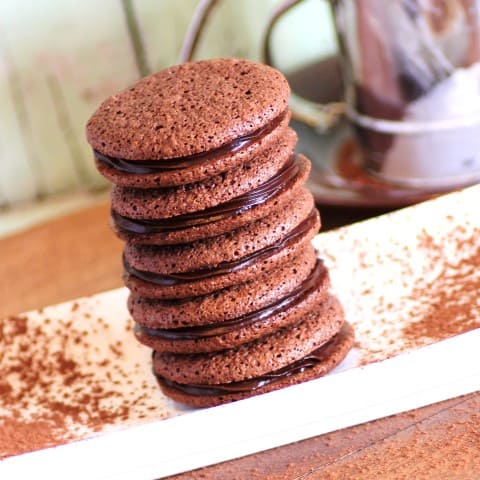 Easy Chocolate Macaroons stacked on a white plate with cocoa powder sprinkled around