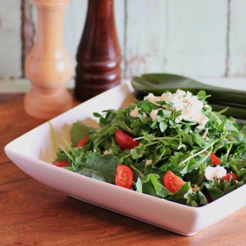 Mixed Baby Kale Salad in a white square bowl on a wooden board