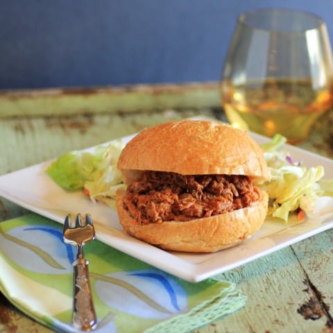 Slow Cooker Pulled Pork Sandwich on a white plate with a glass of white wine