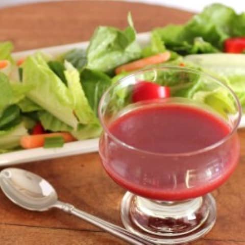 Raspberry Vinaigrette in a small glass bowl with a green salad in the backgorund