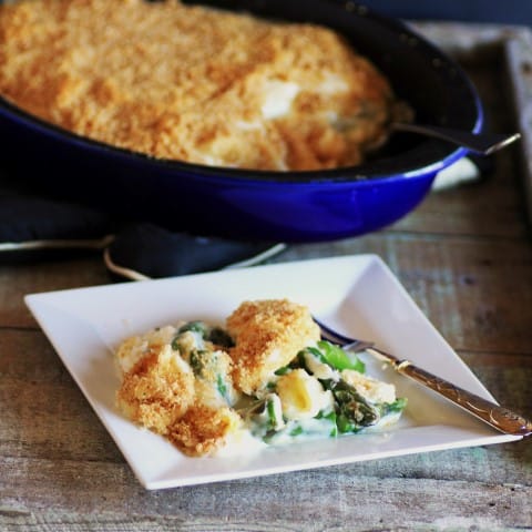 Asparagus and Eggs in Mornay Sauce spooned onto a small white plate from a large blue casserole dish