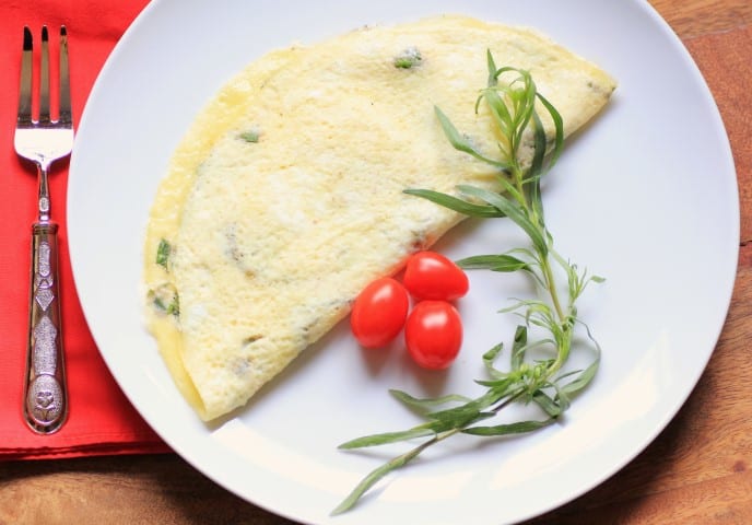 Brie and Herb Omelette on a white plate with fresh tomatoes and a tarragon sprig