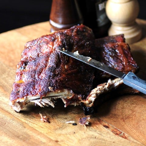 Dry Rubbed Smoked Back Ribs cut in half with a knife sitting on a wooden cutting board