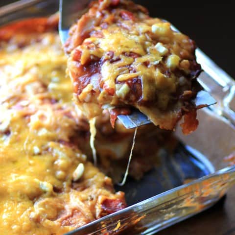 Enchilada Casseroleina glass baking dish and one scoop being spooned out