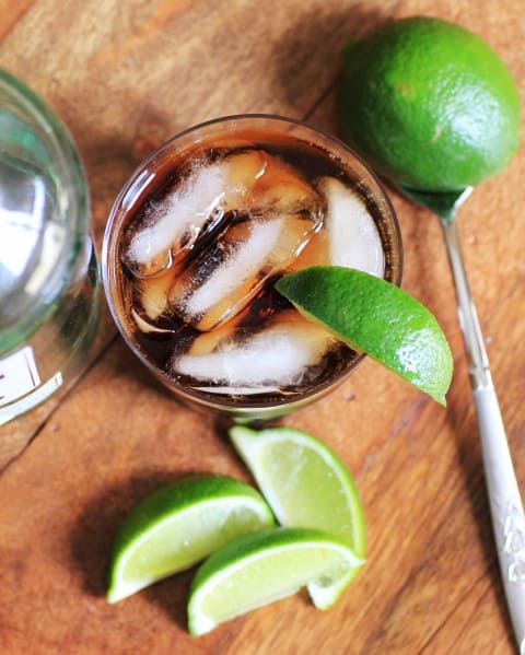 Ginger Root Beer and Rum in a glass with ice and lime wedges on a wooden board