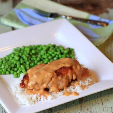 Paprika Chicken on white plate covered with gravy and served over rices with green peas