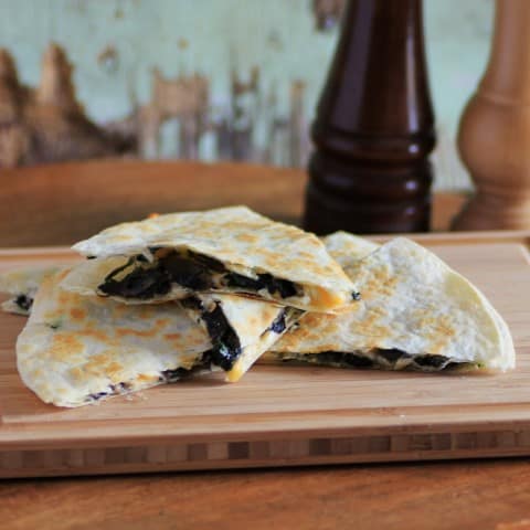 Quesadillas with Mushrooms and Spinach cut in wedges and stacked on a wooden cutting board