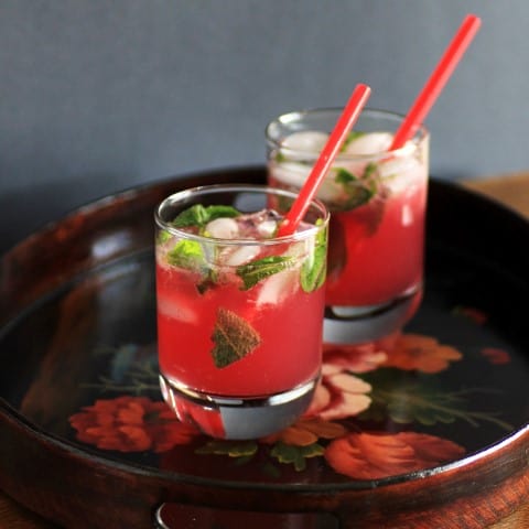 2 Vanilla Pomegranate Mojitos in rocks glasses with red straws ona black serving tray