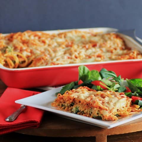 Baked Spaghetti serving on a white plate with the full casserole dish in the background