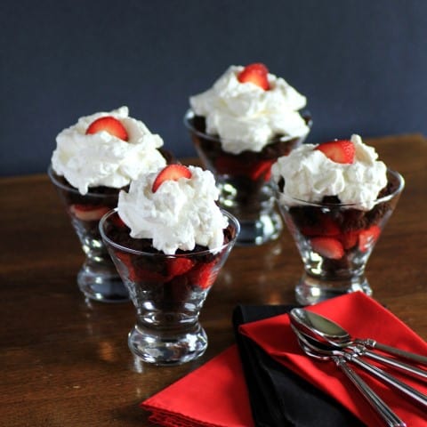 Brownie Delight in glass serving dishes with whipped cream and a sliced strawberry on top