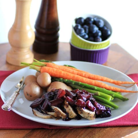 Herbed Pork Tenderloin with Wild Blueberry Sauce sliced on a white plate with carrots, potatoes and asparagus