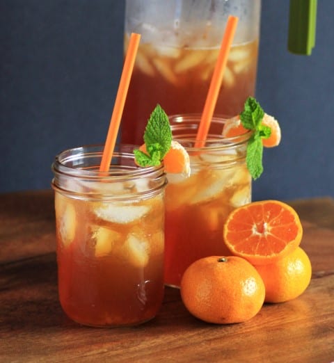 Mandarin Chai Iced Teain mason jars with orange straws and manderin oranges on a wooden cutting board