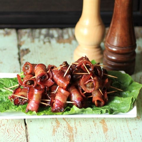 Spicy Caramelized Bacon Wrapped Smoked Oysters on a lettuce leaf on a white serving platter