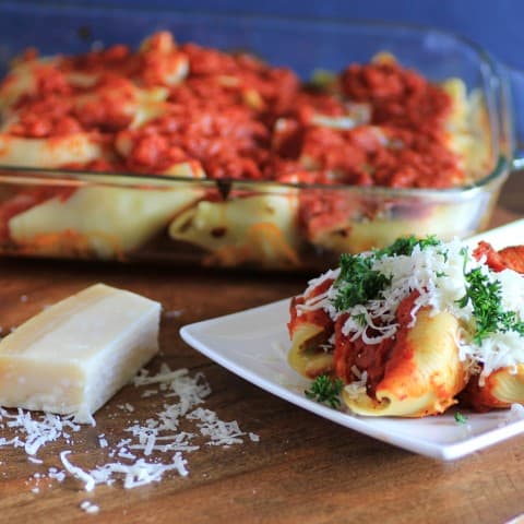 Stuffed Pasta Shells in a casserole dish with one served on a white plate and parmesan cheese beside the plate