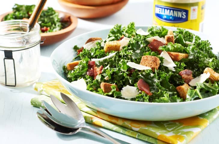 Hellmann's Kale Caesar Salad in a white bowl with serving utencils be side the bowl