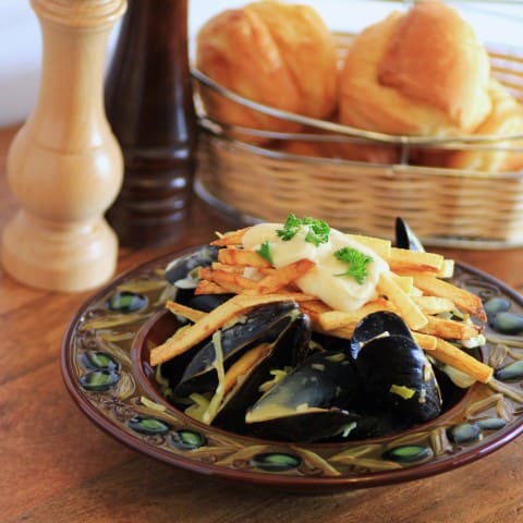 Mussels and Pomme Frites in a brown bowl witha basket of buns in the background